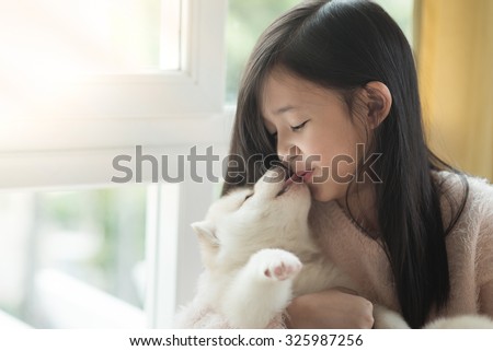 Little asian girl kissing a siberian husky puppy at the window,vintage filter