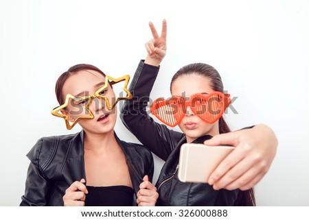Asian girls in the funny sunglasses. They pose, grimace and look at the camera. Hair removed. The skin is clean. They make a picture on the phone. Leather jackets.