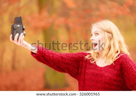 Pretty smiling woman in fall forest park taking selfie self photo with old vintage camera. Happy gorgeous young girl passionate photographer. Autumn winter photography.
