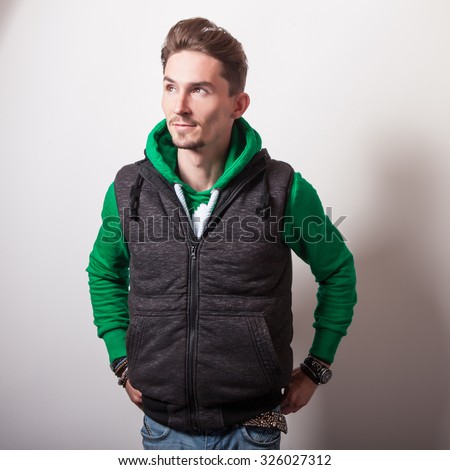 Emotional portrait of attractive young man in a grey vest & green sweater with a hood. Studio photo. 