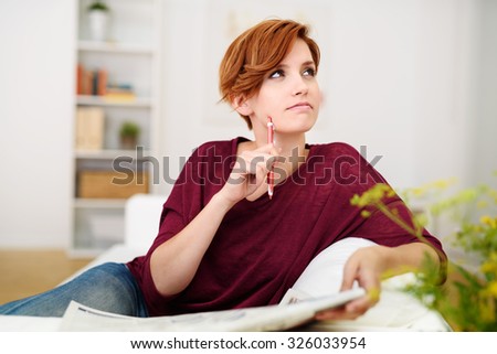 Thoughtful Attractive Young Woman Answering Crossword Puzzle Game on Newspaper at the Living Room Couch. Royalty-Free Stock Photo #326033954