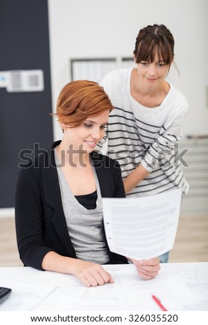 Two Young Office Women Reading a Business Document Together at the Office Table.