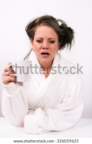 very tired young woman holding a coffee cup and wearing a bathrobe