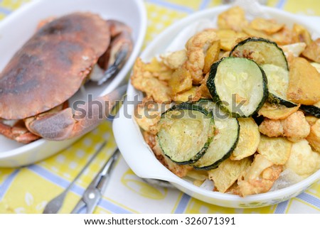 Picture of white dishes with crab and fried vegetables. Tasty dinner on plated tablecloth indoor background.