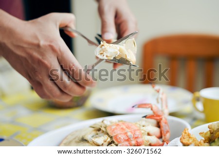 Picture of man's hands cracking lobster claw above dish.  Delicatessen appetizer on restaurant indoor background.