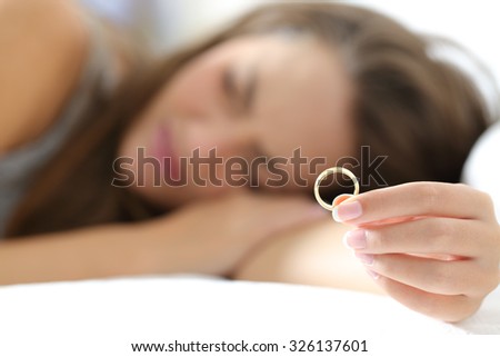Sad wife mourning after divorce holding a wedding ring lying on the bed Royalty-Free Stock Photo #326137601