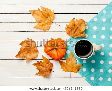 Cup of coffee and pumpkin with leafs on white wooden table