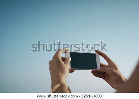 Cropped image of the woman's hands touching a smart-phone display on a sky background