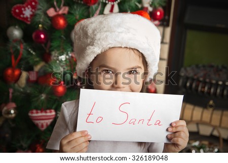 Happy little girl with letter to Santa near christmas tree