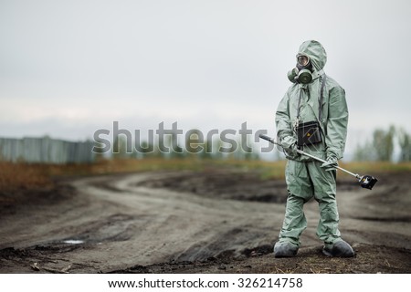 Scientist dosimetrist (radiation supervisor) in protective clothing and gas mask with geiger counter checks the level of radioactive radiation in the danger zone Royalty-Free Stock Photo #326214758