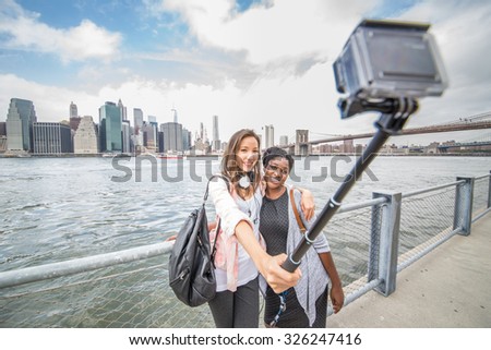 Two female friends taking a picture of New York and Brooklyn Bridge - Best friends traveling and recording their trip with a action camera