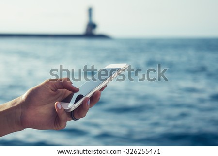 Cropped image of the woman's hands touching a smart-phone display on a sea background