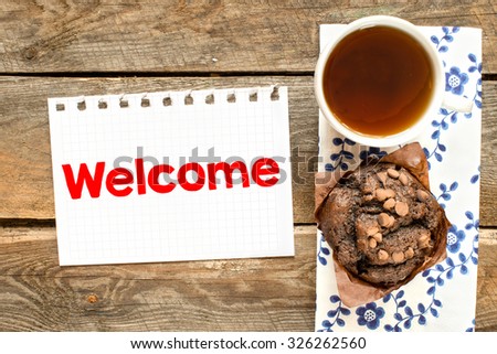 Welcome. Paper sheet with welcome on wooden desk with tea and muffin