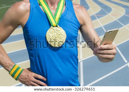 Gold medal athlete standing at running track using his mobile phone
