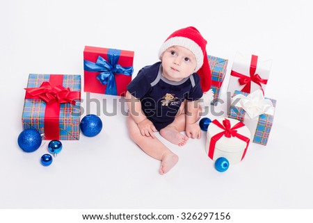 Cute baby sitting among Christmas toys from boxes with gifts and looking at the camera with a smile on his face, picture with depth of field