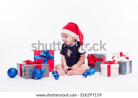 Cute baby sitting among Christmas toys from boxes with gifts and looking at the camera with a smile on his face, picture with depth of field
