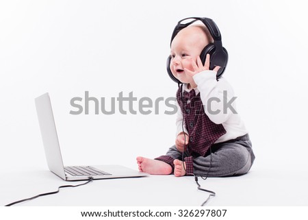 Cute baby sitting in front of a laptop wearing headphones on a white background smiling and listening to music, picture with depth of field