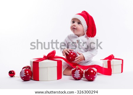 beautiful baby in the New Year's cap and white body sits among boxes of holiday gifts and Christmas balls, picture with depth of field