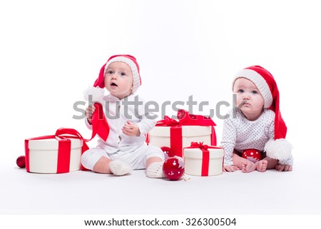Two beautiful baby in the New Year's cap and white body sitting among festive boxes with gifts and Christmas balls, picture with depth of field