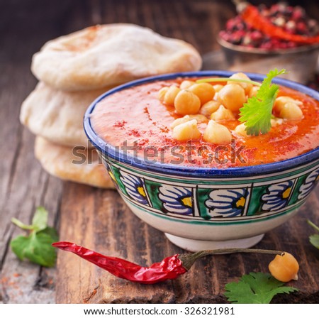 Cream soup puree of roasted tomatoes and peppers served with chickpeas cilantro in a blue ceramic bowl, served with pita flat bread on a dark wooden background. selective Focus