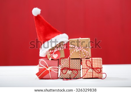 Christmas little gift boxes with Santa hats on red colored wooden board