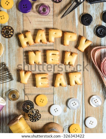 ABC Cookie in the form of word HAPPY NEW YEAR and sewing tools on vintage wooden background. Copy-Space