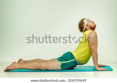 Funny picture of red haired, bearded, plump man on white background. Man wearing sportswear. Man is lying on the mat, he trains.