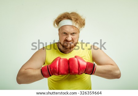 Funny picture of red haired, bearded, plump man on white background. Man wearing sportswear and red boxing gloves. He is angry 