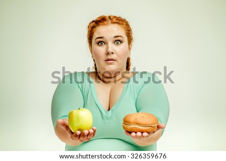 Funny picture of amusing, red haired, chubby woman on white background. Woman holding apple and sandwich. She is surprised
