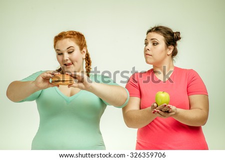 Funny picture of amusing chubby women on white background. One woman holding a sandwich, the other holding an apple.