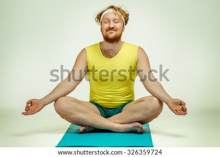 Funny picture of red haired, bearded, plump man on white background. Man wearing sportswear. Man sitting on the mat, he is meditating