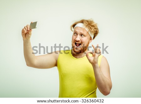 Funny picture of red haired, bearded, plump man on white background. Man wearing sportswear. Man smiling and taking a selfie 