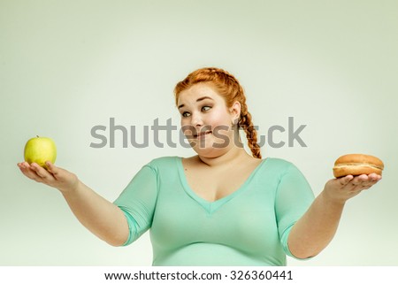 Funny picture of amusing, red haired, chubby woman on white background. Woman holding apple and sandwich.  She is looking at an apple 