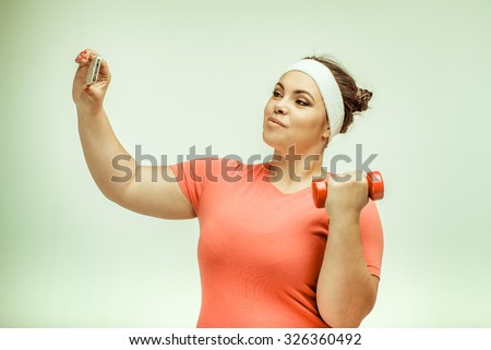 Funny picture of amusing chubby woman on white background. Woman taking a selfie and holding a dumbbell