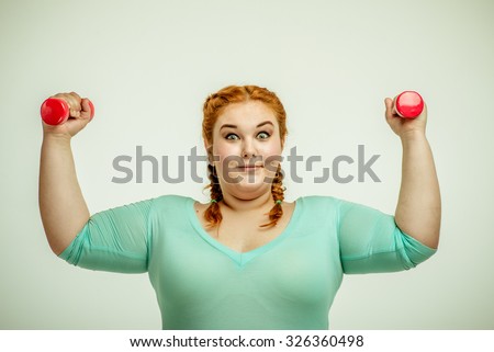 Funny picture of amusing, red haired, chubby woman on white background. Woman smiling and holding dumbbells