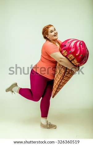 Funny picture of amusing, red haired, chubby woman on white background. Woman holding a huge ice cream 