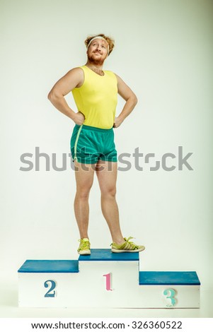 Funny picture of red haired, bearded, plump man on white background. Man wearing sportswear. He is standing on a pedestal