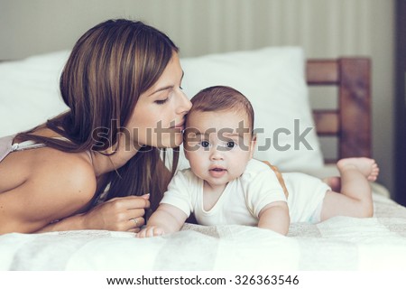 Portrait of beautiful mother kissing her 5 months old baby in the bed