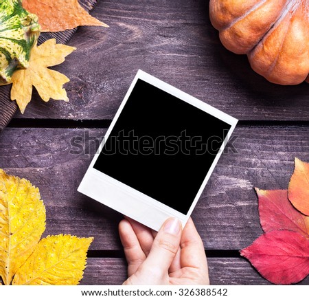 Hand holding retro photo near autumn leaves and pumpkin on wooden background  