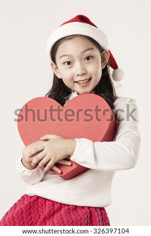 A asian(japanese, korean, chinese) girl(kid, children) hold a red heart(love) gift box for christmas(xmas) at the studio.