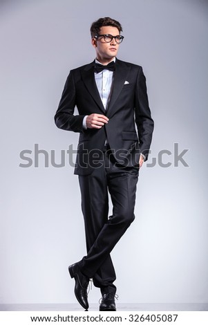 Business man standing on studio background with his legs crossed while opening his jacket. Royalty-Free Stock Photo #326405087