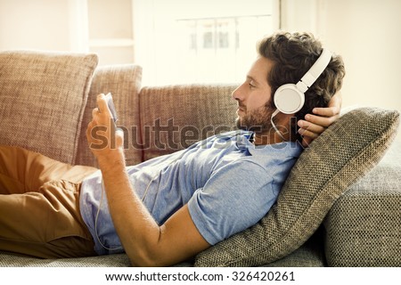 Man on couch watches a movie on mobile phone Royalty-Free Stock Photo #326420261