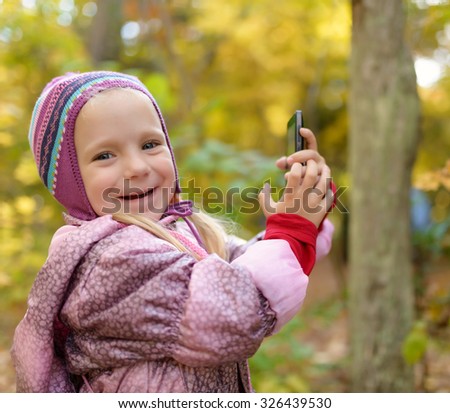 Little girl making photo or video with smartphone in the forest. Selective focus with shallow depth of field.