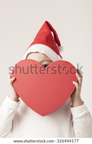 A boy look at the camera with heart shaped gift box and wearing christmas hat for xmas at the studio.