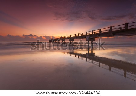 Beautiful sunrise seascape with amazing reflection on the sand. Soft focus and motion blur due to long exposure.