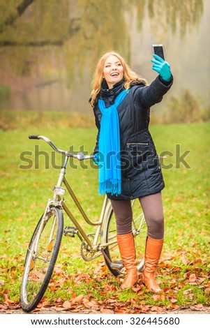 Happy active woman with bike bicycle in fall autumn park taking selfie self photo picture. Glad young girl in jacket and scarf relaxing. Healthy lifestyle.