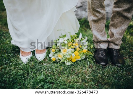 bride and groom standing on green grass next to a bouquet of white and yellow flowers with green
