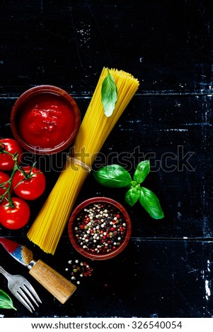 Background with italian food (pasta, basil leaves, spices, herbs and tomato sauce) on dark vintage board. Top view. Vegetarian food, diet, health or cooking concept.