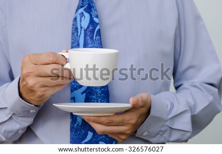 Businessman in blue shirt and necktie holding cup of coffee, close up.