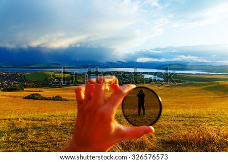 Beautiful landscape, green and yellow meadow and lake with mountain in background. People in polarization filter in man hand Royalty-Free Stock Photo #326576573